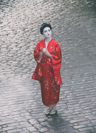 Portrait of a woman in geisha makeup standing on a cobblestone pavement