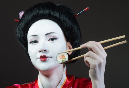 Woman in geisha makeup eating sushi, gray backgroundの写真素材