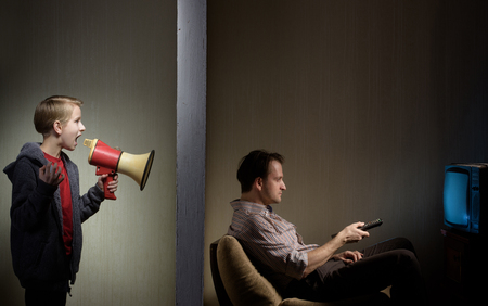 Man watching TV while his son calling him through a megaphone. Lack of father's attention conceptの写真素材