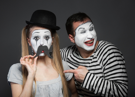 Female mime with paper mustaches, male mime laughing at herの写真素材