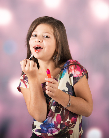Portrait of a beautiful little lady applying lip gloss, abstract backgroundの写真素材