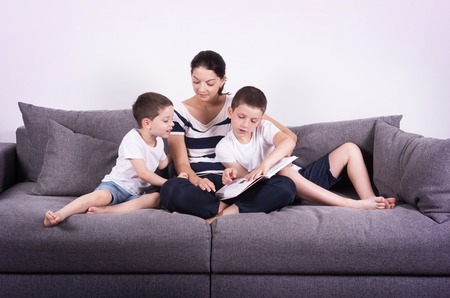 Mother reads an interesting book with her sons of the sofa. Studio portrait on white background.の写真素材