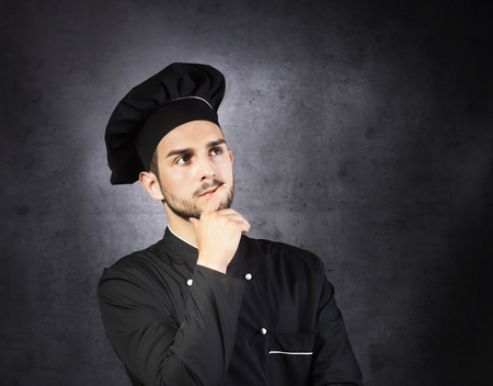 Portrait of a thinking chef cooker in black uniform, gray backgroundの写真素材