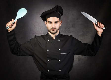Portrait of a chef cooker with knife and spoon in black uniform, gray backgroundの写真素材
