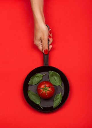 Fresh tomato on frying pan with basilic. Isolated on red background.の写真素材