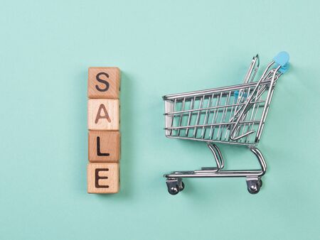 A miniature shopping cart and wooden blocks with the wordings SALE, isolated against mint background.の写真素材