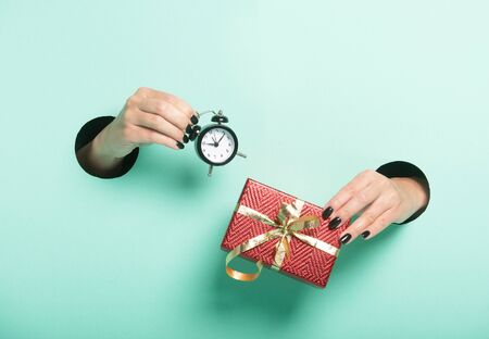 Female hands hold red gift and alarm clock through a hole on mint background. Isolated sale concept.