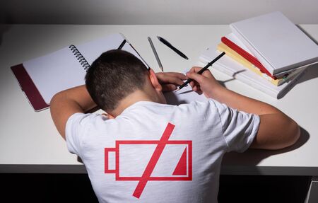 Bored and tired boy doing homework on white desk in his room. Schoolboy probems concept. ISo