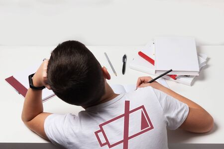 Bored and tired boy doing homework on white desk in his room. Schoolboy probems concept. ISo