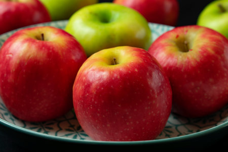 Ripe red apples in a plate on a dark background close up
