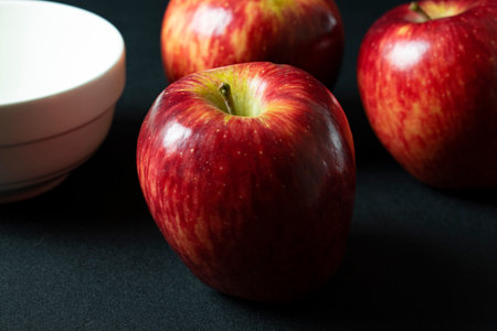 Red apples on a black background with a white bowl in the backgroundの写真素材