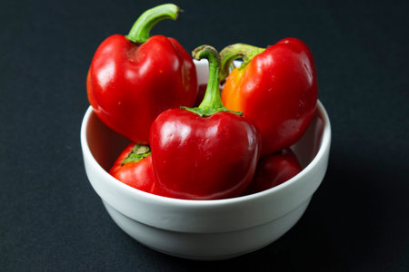 Red and yellow bell peppers in a white bowl on a black backgroundの写真素材