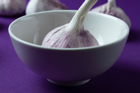 Garlic in a white bowl on a purple background, close upの写真素材