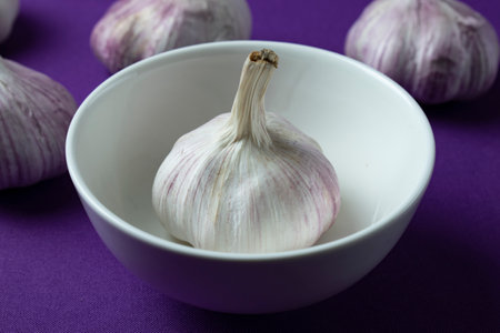 Garlic in a white bowl on purple background, close-upの写真素材