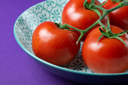 Ripe red tomatoes on a branch in a bowl on a purple backgroundの写真素材