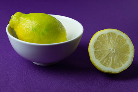 Lemon and lemon slices in a white bowl on a purple backgroundの写真素材