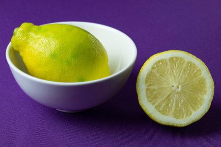 Lemon and lemon slices in a white bowl on a purple backgroundの写真素材