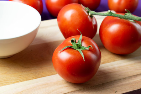 Tomatoes on a cutting board with a white bowl in the backgroundの写真素材