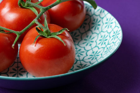 Cherry tomatoes on the vine in a plate on a purple backgroundの写真素材