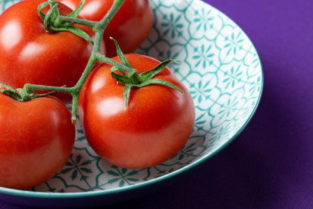 Ripe red tomatoes in a plate on a purple background close upの写真素材