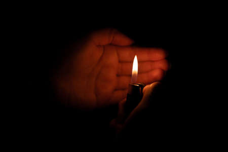 Lit cigarette lighter in one hand in the darknessの写真素材