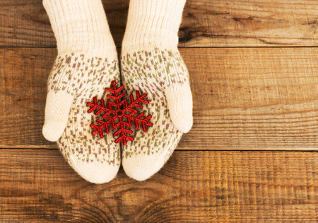 Woman hands in light teal knitted mittens are holding snowflake on wooden background. Winter and Christmas concept.の写真素材