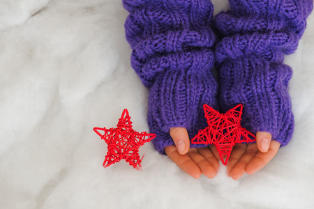 Woman hands in light teal knitted mittens are holding red stars on snow  background. Winter and Christmas concept.の写真素材