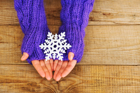Woman hands in light teal knitted mittens are holding snowflake on wooden background. Winter and Christmas concept.の写真素材