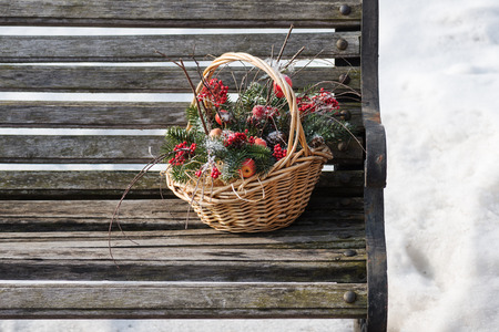 Composition of fir branches, rowan and apples in wicker basket on a background of snow and the old bench.の写真素材