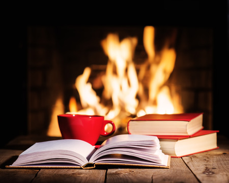Red cup of coffee or tea and old books on wooden table near  fireplace. Winter and Christmas holiday concept.の写真素材