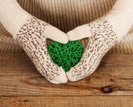 Woman hands in light teal knitted mittens are holding heart on wooden background. Winter and Christmas concept.の写真素材