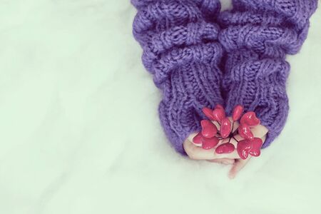 Woman hands in light teal knitted mittens are holding hearts on snow background. Winter and Christmas concept.の写真素材