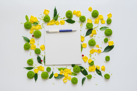 Sheet of paper and pen with pattern from petals of chrysanthemum flowers, ficus leaves and ripe rowan on white background. Overhead view. Flat lay.の写真素材