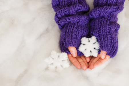 Woman hands in light teal knitted mittens are holding snowflakes on snow background. Winter and Christmas concept.の写真素材