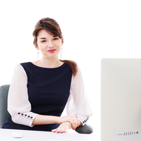 Portrait of young pretty business woman in white and blue suit looking on screen of computer sitting at her workplace in office.の写真素材