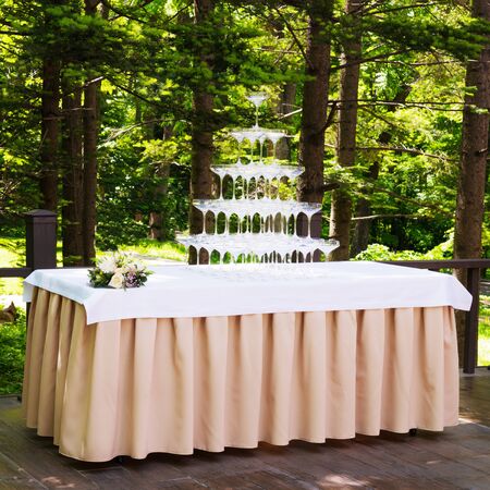 Empty wine or champagne glasses on table are in pyramid. Tower of glasses at wedding ceremony outdoors.の写真素材