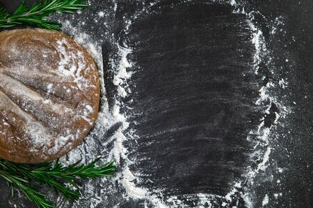 Loaf of bread with flour and rosemary on black background. Slate concept with copy space.の写真素材