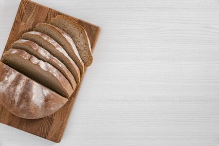 Sliced loaf of bread on rectangular wooden cutting board on white background top view.の写真素材