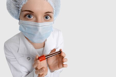 Isolated nurse on white background in medical mask with blood sample for Coronavirus testing looks at you fearfully. Epidemic Middle East Respiratory Syndrome 2019-nCoV.の写真素材