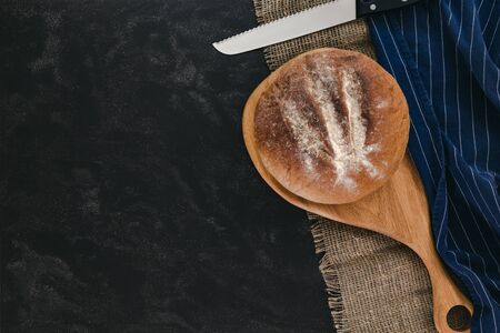 Whole bread on wooden board and canvas, with blue striped textile on black marble background, top view.の写真素材