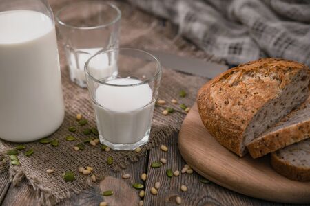 Milk and whole wheat bread with scattered seeds and nuts on an old planked table with sackcloth.の写真素材