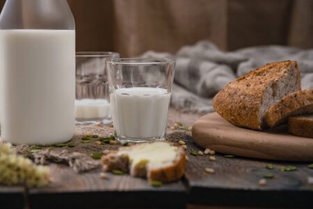 Breakfast in the country with milk and whole wheat bread. Sliced and bitten bread with butter on an old vintage planked wooden table with canvas.の写真素材