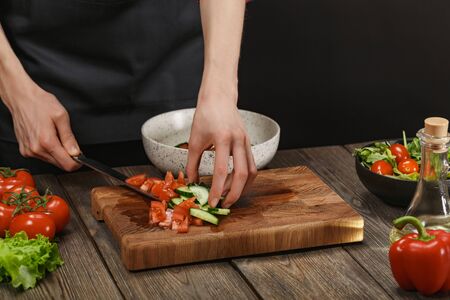 Woman cooking fresh salad. Female hands cutting vegetables on board on wooden table.の写真素材
