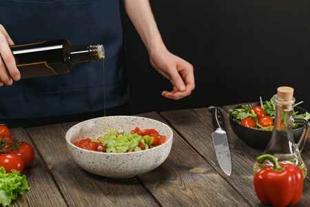 Woman cooking healthy food on wooden table. Female hands adding olive oil into bowl with vegetable salad. Diet concept for healthy lifestyle.の写真素材