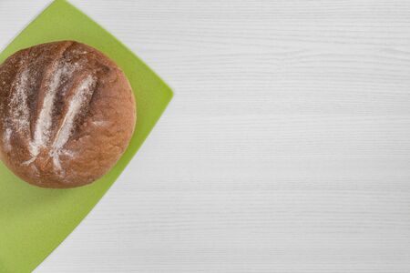 Round loaf of bread on green cutting board on white background top view.