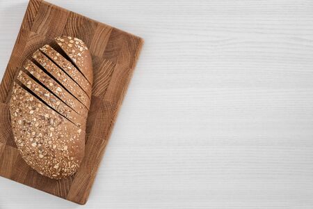 Bread with seeds and flakes on rectangular wooden cutting board on white background top view.の写真素材