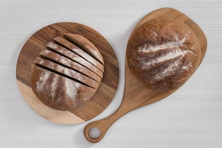 Two loaves of bread, whole and sliced, on wooden cutting boards on white background top view.の写真素材