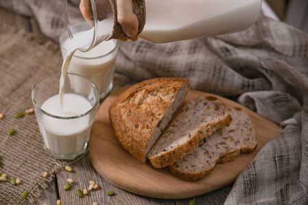 Breakfast in the country with milk and whole wheat bread. Sliced bread on an old vintage planked wooden table with canvas.の写真素材