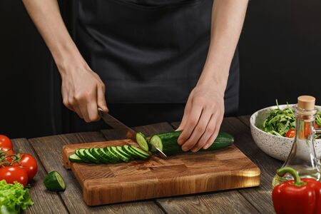 Woman cooking fresh salad. Female hands cutting vegetables on board on wooden table.の写真素材