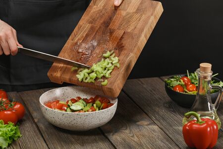 Woman cooking fresh salad. Female hands cutting vegetables on board on wooden table.の写真素材